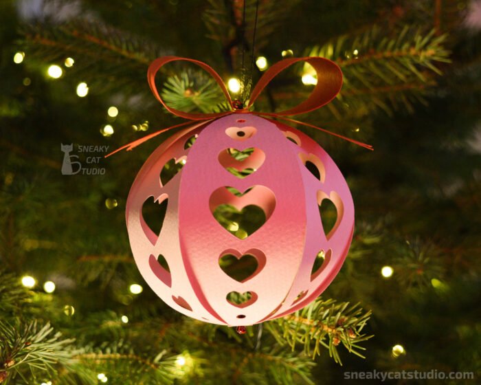 Pink paper Christmas ball with heart pattern on the Christmas tree with light front view