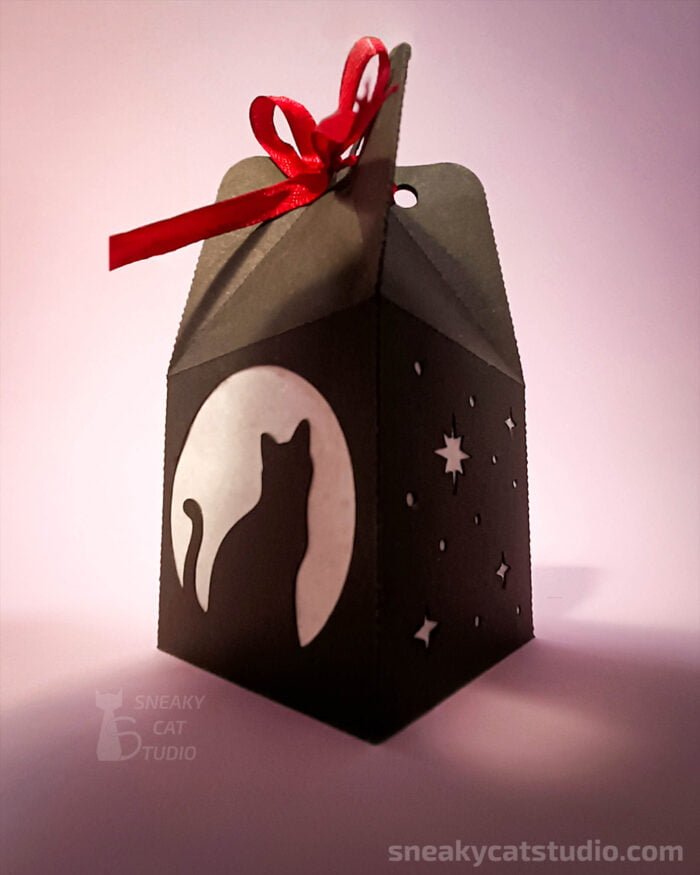 Paper black box with cat, moon and stars pattern on pink background side view